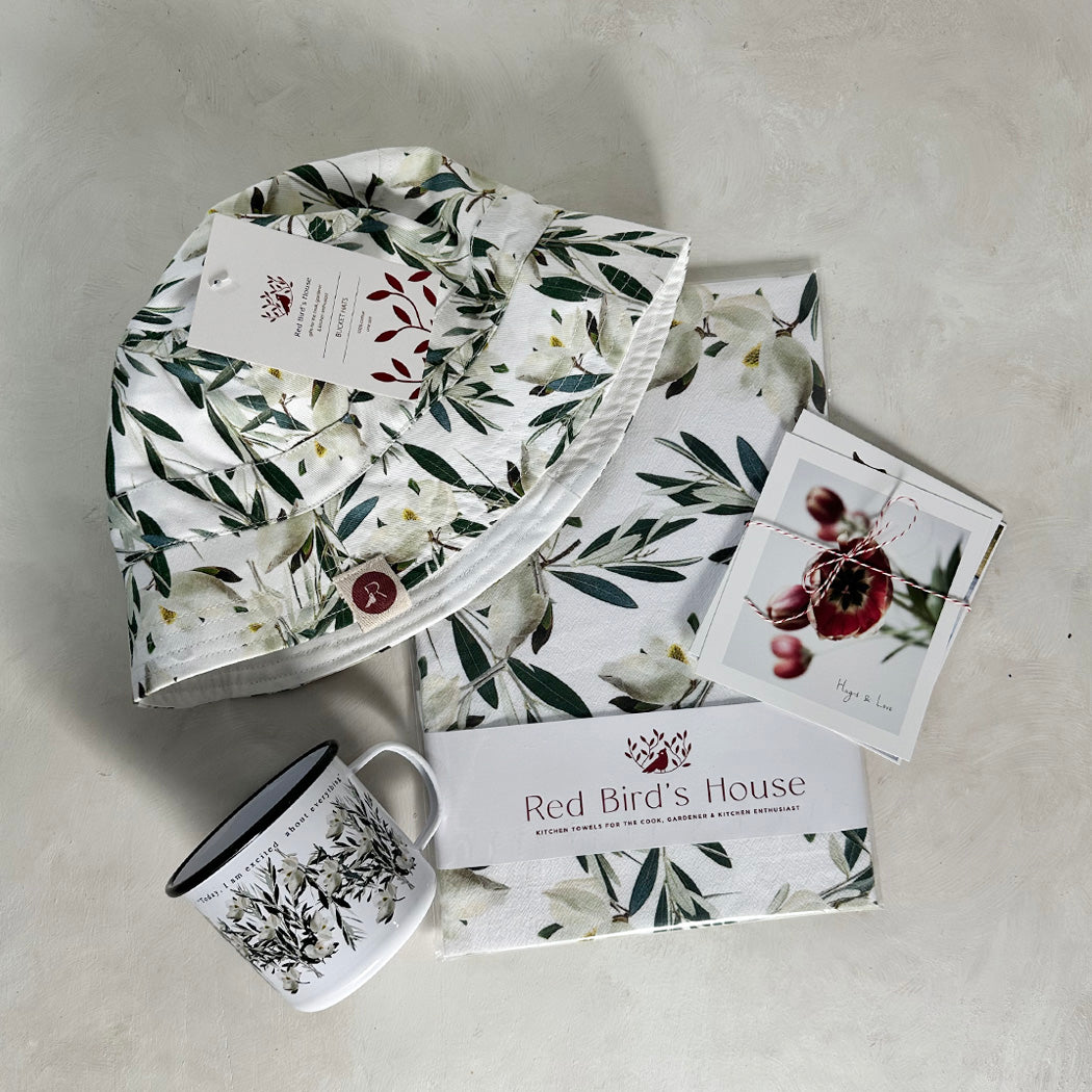 A beautiful and clean design with magnolias and olive branches gives this set a contemporary look.&nbsp;  Gift set includes matching 1 kitchen towel, 1 hat and 1 enamel cup by Red Bird's House