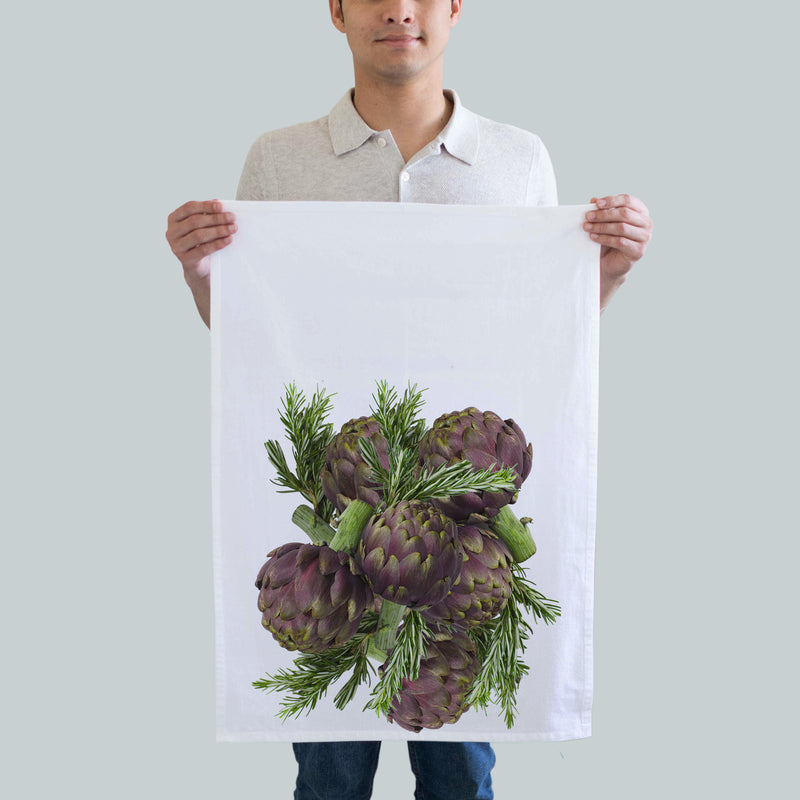 A kitchen towel printed with a collage of artichokes and Rosemany leaves.  In tones of purple and green.  size 18x29, print size 16x18 inches.
