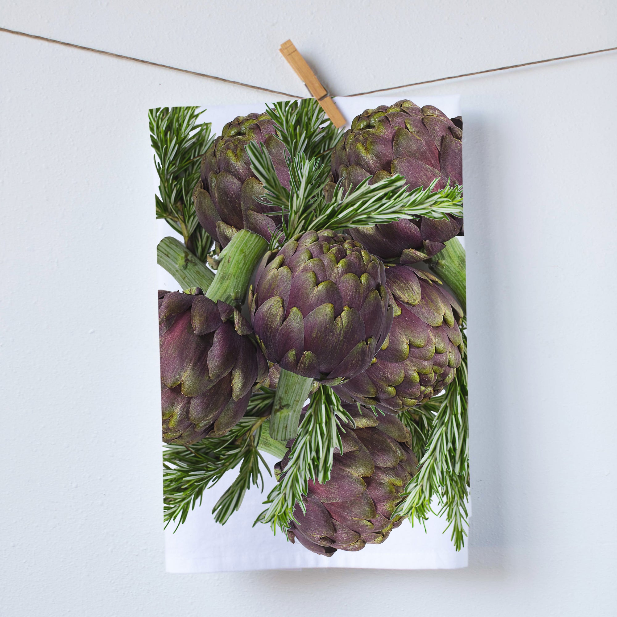A kitchen towel printed with a collage of artichokes and Rosemany leaves.  In tones of purple and green.  size 18x29, print size 16x18 inches.